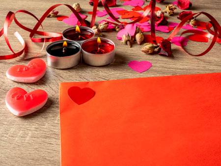 red envelope next to candles with red rose petals and hearts on the tableの写真素材