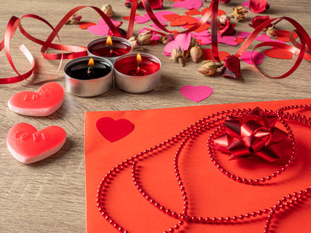 red envelope next to candles with red rose petals and ribbon on the tableの写真素材