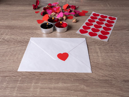 white envelope next to candles with red rose petals and hearts on the tableの写真素材