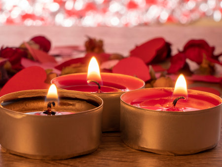 red envelope next to candles with red rose petals and ribbon on the tableの写真素材