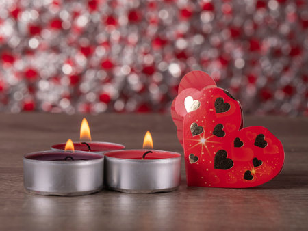 red envelope next to candles with red rose petals and ribbon on the tableの写真素材