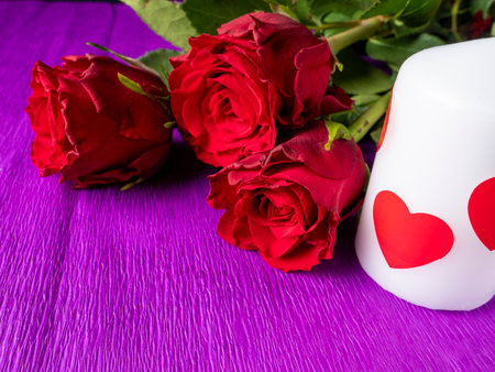 Red roses with a white candle on which a red heart, on a purple backgroundの写真素材