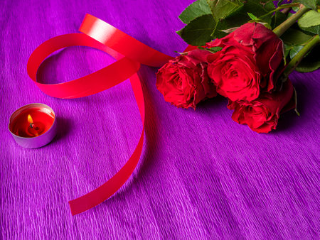 red roses with ribbon and burning candle on purple backgroundの写真素材