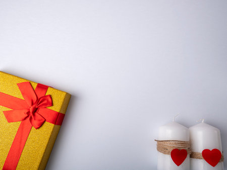 A yellow gift with a ribbon in the shape of a butterfly knot lies next to two white candles which are on a bright white backgroundの写真素材