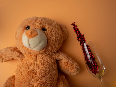 A large brown teddy bear lies next to a glass with sparkles on an orange backgroundの写真素材