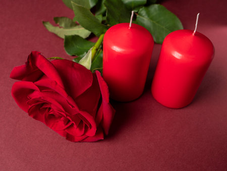 A large red rose which is next to two red large candles which are on a red backgroundの写真素材