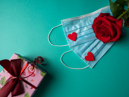 Two blue masks with two red hearts and a red rose on the masks, and a pink gift on a green backgroundの写真素材