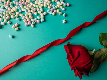 Red rose and multicolored candies and between them lies a red long ribbon on a green backgroundの写真素材