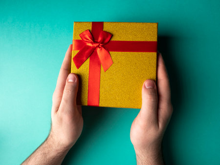Yellow gift with a red ribbon butterfly knot which is in the hands on a green backgroundの写真素材