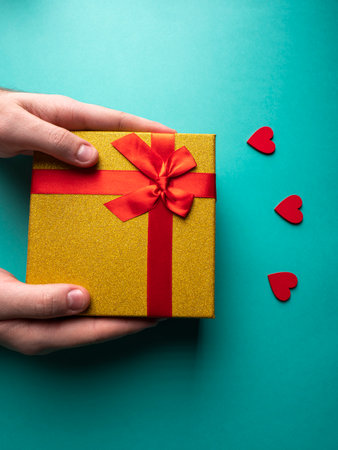 Yellow gift with a red ribbon butterflies knot which is in the hands, and near 3 red hearts, on a green backgroundの写真素材
