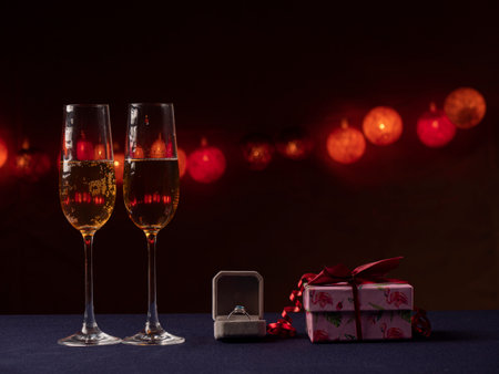 Two glasses of champagne, a white box with a ring and a pink gift next to a black background with lightの写真素材