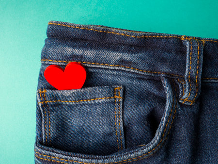 Blue jeans and one red heart lies in the front pocket of jeans on a green backgroundの写真素材
