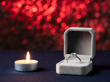 A white candle that burns and next to it is a box with a ring with a blue stone, on a pink backgroundの写真素材