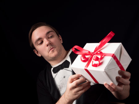 a young guy in a black t-shirt suit hold with surprise a gift on a black backgroundの写真素材