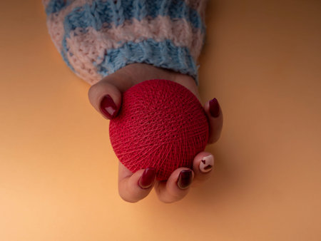 Stylish female manicure. Young female hand in a woolen sweater hold a red ball. nails with red...