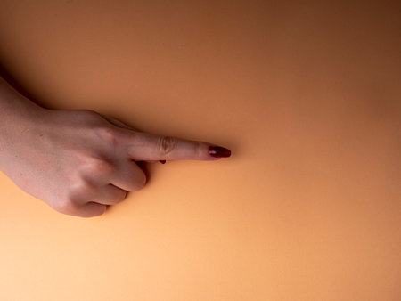 Stylish female manicure. Young female hands show one index finger with red manicure, on an orange background. Manicure at home during a pandemicの写真素材