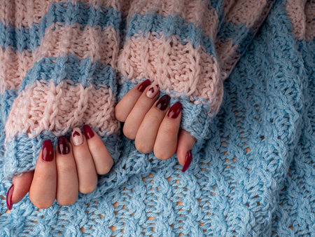 Stylish female manicure. Young female hands hold woolen material. nails with red manicure and white with hearts, on an blue wool background. Manicure at home during a pandemicの写真素材