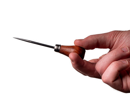 a metal awl for leather with a brown handle is in a man's hand. Hand tool, metal awl and hand isolated on white backgroundの写真素材