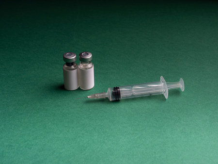 Two glass vials in which a liquid with a vaccine stand and a syringe lies next to it. Glass vials...