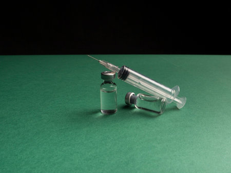 Two glass vials in which a liquid with a vaccine stand and a syringe lies next to it. Glass vials and syringe on green and black backgroundの写真素材