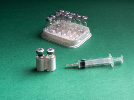 Glass vials in which the liquid with the vaccine is in the tray of the automatic liquid dispenser, and there is a syringe on it. Glass vials and syringe are on a green backgroundの写真素材