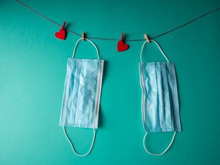 two blue medical masks that weigh on a rope with two red hearts fixed with clothespins on a green backgroundの写真素材