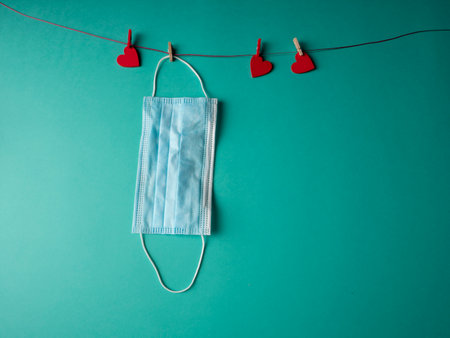 A blue medical mask that weighs on a rope with three red hearts fixed with clothespins on a green backgroundの写真素材