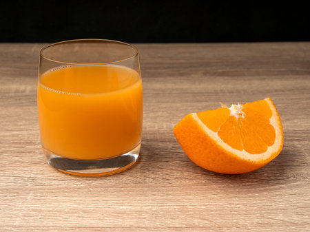 Glass glass with orange juice and orange stand on a wooden gray table on a dark background Fresh...