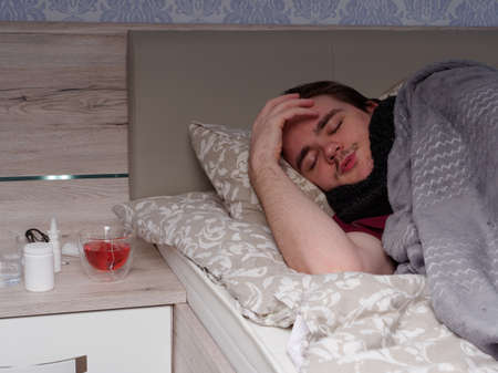 young guy sleeping in bed in the bedroom after taking cold medicine, he is sick, concept of illness at homeの写真素材