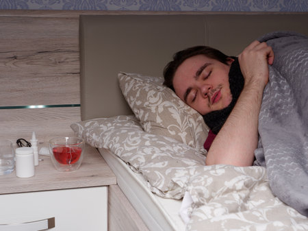 young guy sleeping in bed in the bedroom after taking cold medicine, he is sick, concept of illness at homeの写真素材