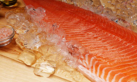 Fillet of fresh raw salmon lies on ice and next to spices, which is on a cutting wooden board. Macro photo. Healthy food conceptの写真素材