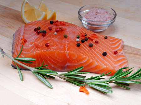 Close-up of slice of red fresh raw salmon fillet with pepper and spices and rosemary next to it. lie on a wooden cutting board. Healthy food conceptの写真素材