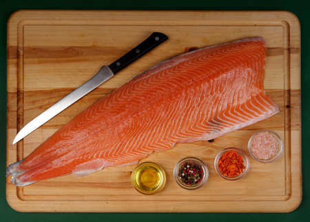 Flatlay of Fillet of fresh raw salmon, a carving knife and spices next to it, which is on a cutting wooden board. Healthy food conceptの写真素材