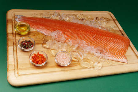 Fillet of fresh raw salmon lies on ice and next to spices, which is on a cutting wooden board. Healthy food conceptの写真素材