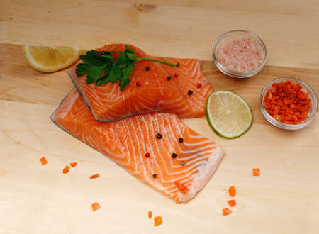 Close-up of two slices of red fresh raw salmon fillet with parsley and spices and lemon next to it. lie on a wooden cutting board. Healthy food conceptの写真素材