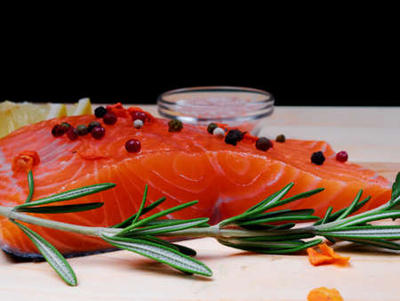 Close-up of slice of red fresh raw salmon fillet with pepper and spices and rosemary next to it. lie on a wooden cutting board. Focus on rosemary and salmon. Healthy food conceptの写真素材