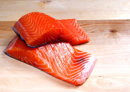 Close-up of two slices of red fresh raw salmon fillet lie on a wooden cutting board.の写真素材