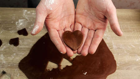 A young chef holds a heart made of ginger dough in his hand, dough and other forms in the background. Baking conceptの写真素材