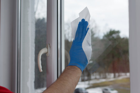 A male hand in blue gloves holds a white paper on the glass. Window cleaner conceptの写真素材
