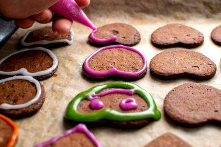 A young chef decorates the gingerbread cookies with pink icing, draws the eyes and mouthの写真素材