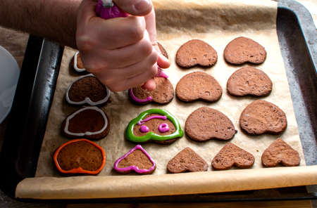 A young chef decorates the gingerbread cookies with pink icing, draws the eyes and mouthの写真素材