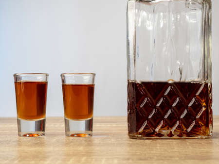 Alcohol is poured into glasses and a decanter stands in a row, all this is on a wooden table on a white background, the concept of relaxation with alcohol.の写真素材