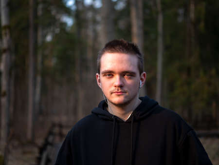 A guy in a black tracksuit, a portrait on a forest background, the sun at sunset, the guy goes in for sports, the concept of a healthy lifestyle.の写真素材