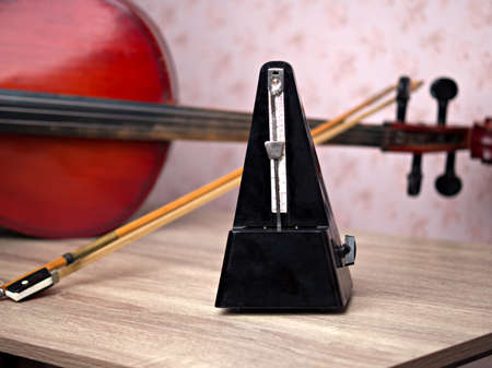 A black vintage metronome beats the rhythm while standing on the table, a cello is lying behind, a close-up shot Musical instrument concept.の写真素材