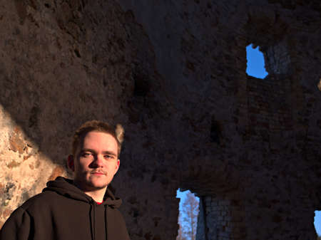 Young guy in a black tracksuit on the street, smiles and looks towards the sun, he's inside an old mill, sports life concept.の写真素材
