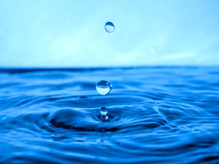 A blue drop drips into the water and creates splashes of various shapes, waves are created through the water, the concept of a liquid splash, a substance painted in blue colorの写真素材