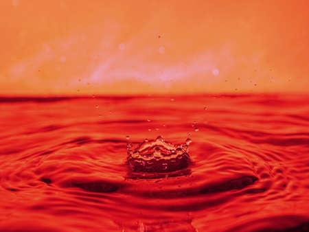 A red drop drips into the water and creates splashes of different shapes, due to the splashes waves are created on the water, the concept of a liquid splash, the substance is painted pinkの写真素材