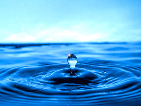 A blue drop drips into the water and creates splashes of various shapes, waves are created through the water, the concept of a liquid splash, a substance painted in blue colorの写真素材
