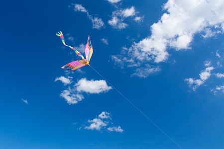 Rainbow kite flies in the blue sky among the cloudsの写真素材
