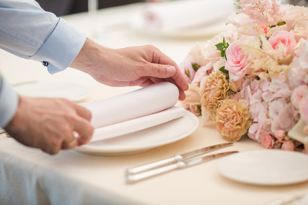 Waiters is serving dinner place on a wedding in a restaurant. Table decorated with flowersの写真素材